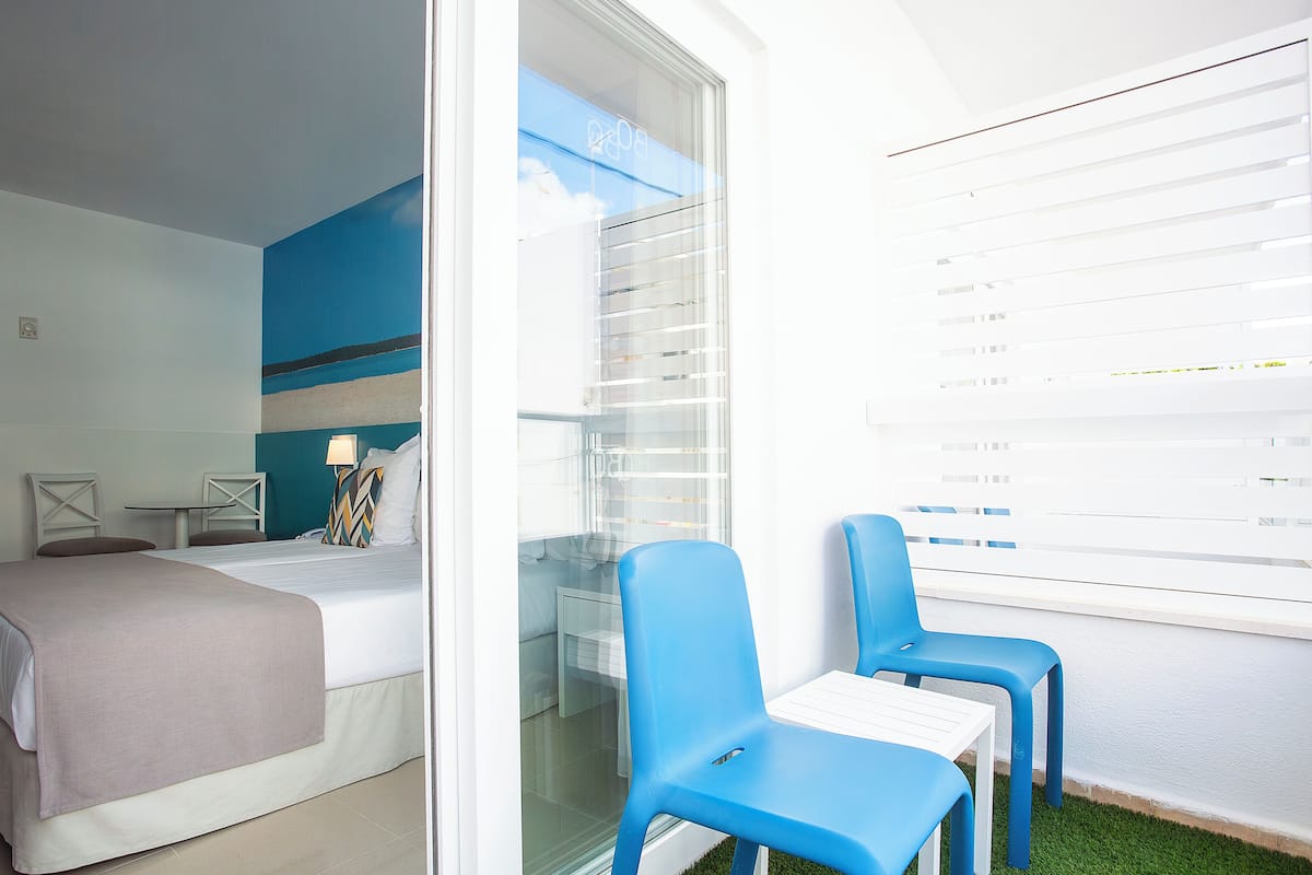 Une chambre d’hôtel avec un lit, une petite table, deux chaises, une porte vitrée et une vue sur l’extérieur.
