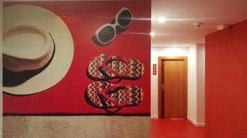 Un pasillo con una pared roja, una puerta marcada con el número 406 y un adorno de pared que muestra un sombrero y chanclas.