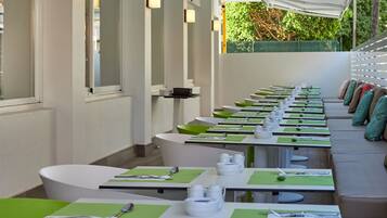 Un comedor con mesas largas, manteles individuales verdes y vajilla blanca.