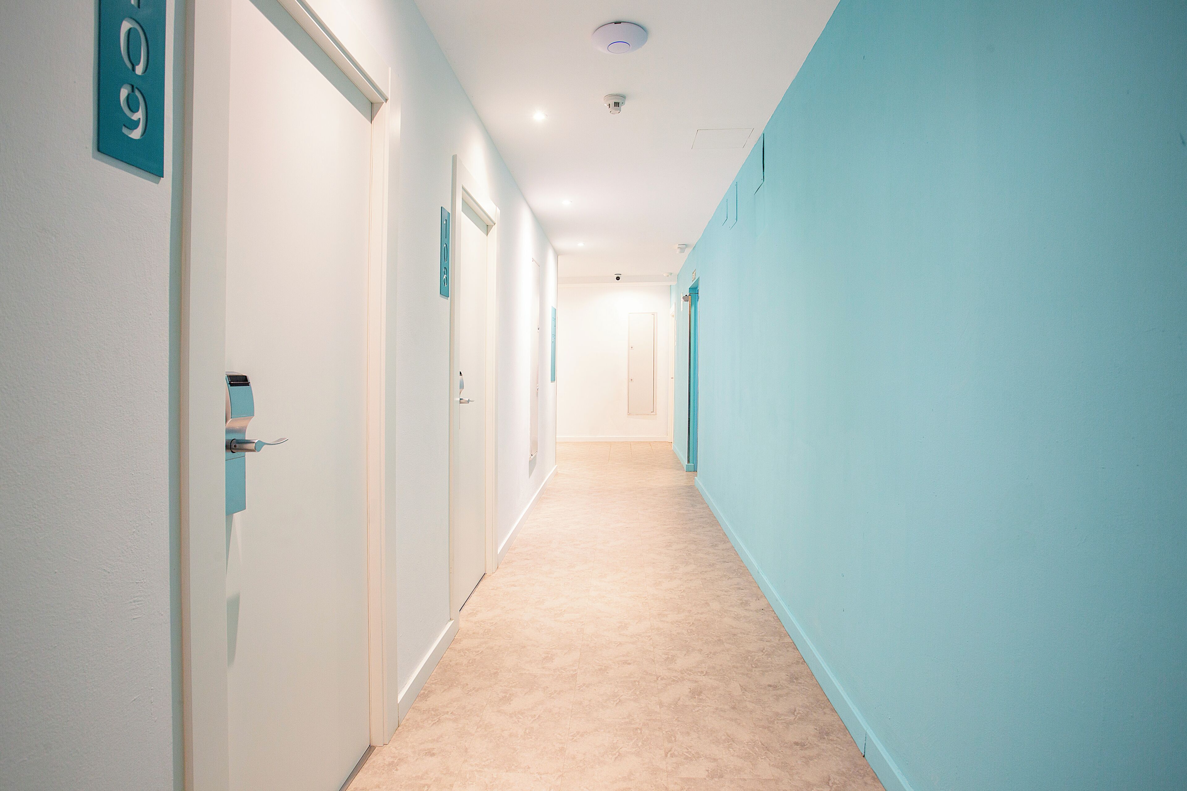 Un couloir avec les portes numérotées 9 et 10, un tapis beige et des murs bleu clair.