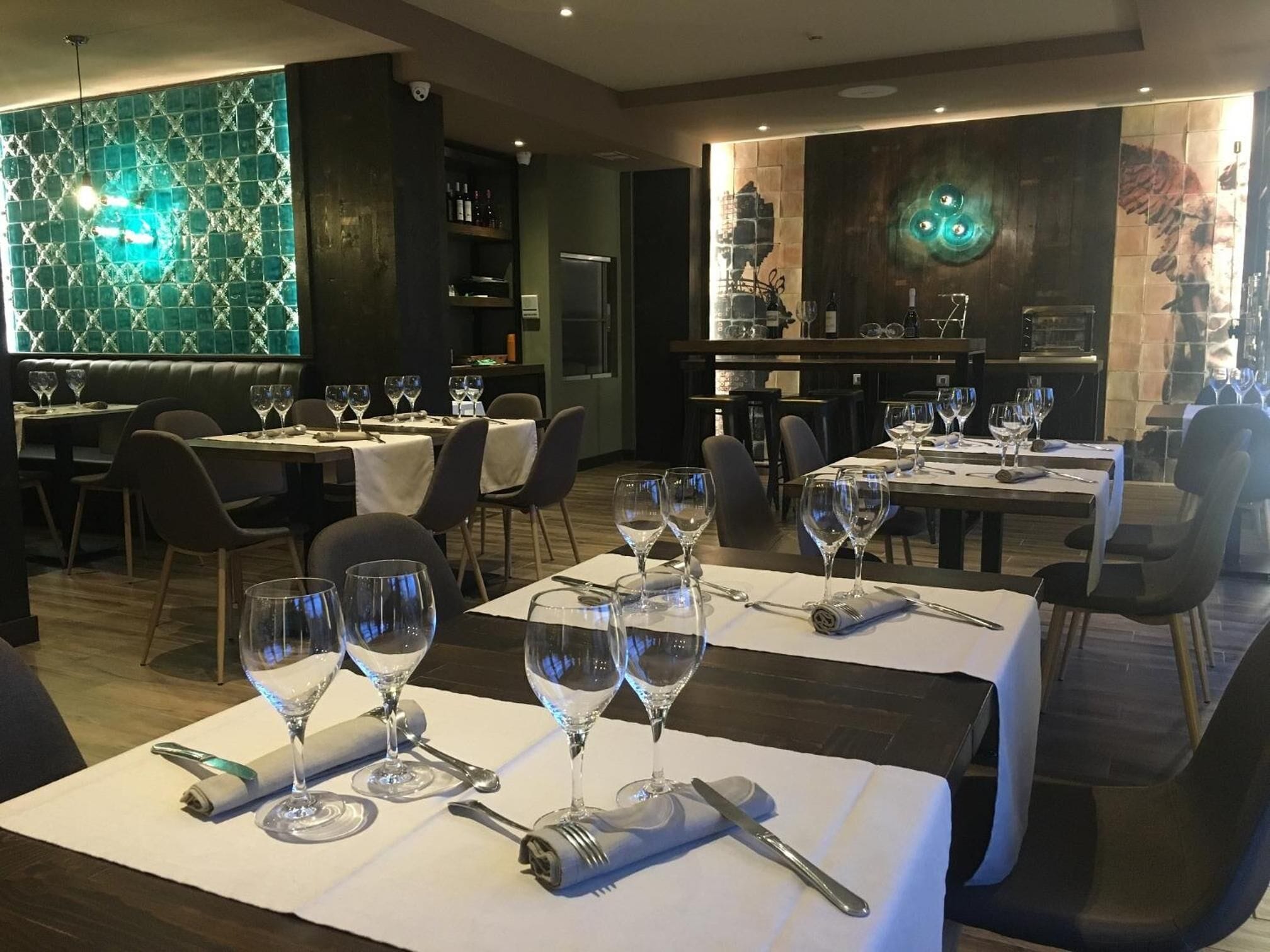 Un restaurante con varias mesas dispuestas para comer, cada una con copas de vino y cubiertos.