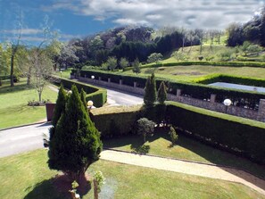 A well-maintained garden with neatly trimmed hedges, a paved pathway, and a variety of trees. - Hotel Comillas (Comillas)