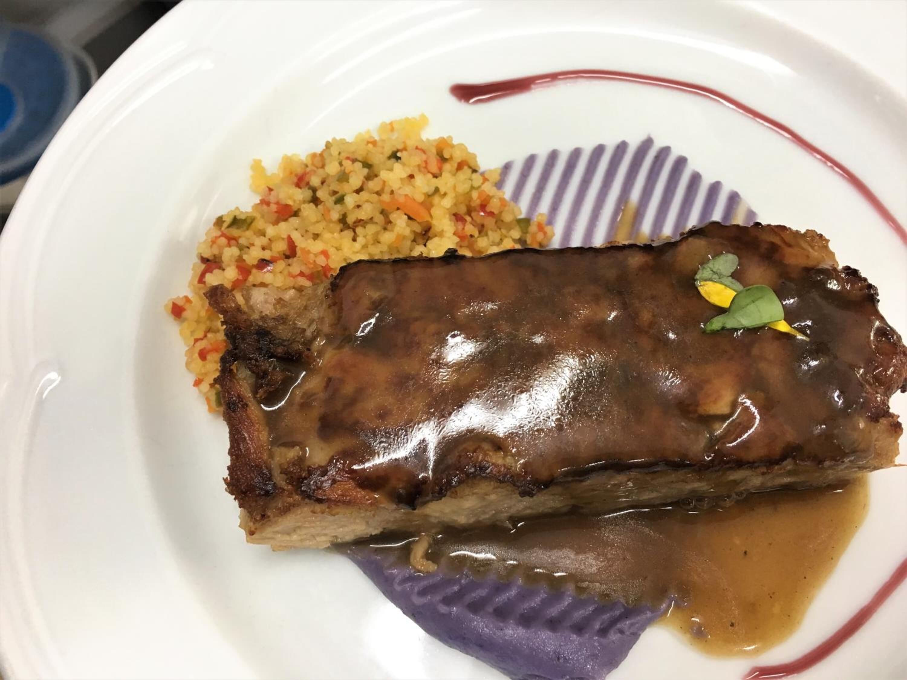 Un plato con un trozo de carne bañado en salsa, acompañado de arroz y una guarnición morada.