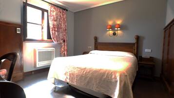 A bedroom with a bed, a radiator, a chair, and a wall-mounted lamp.