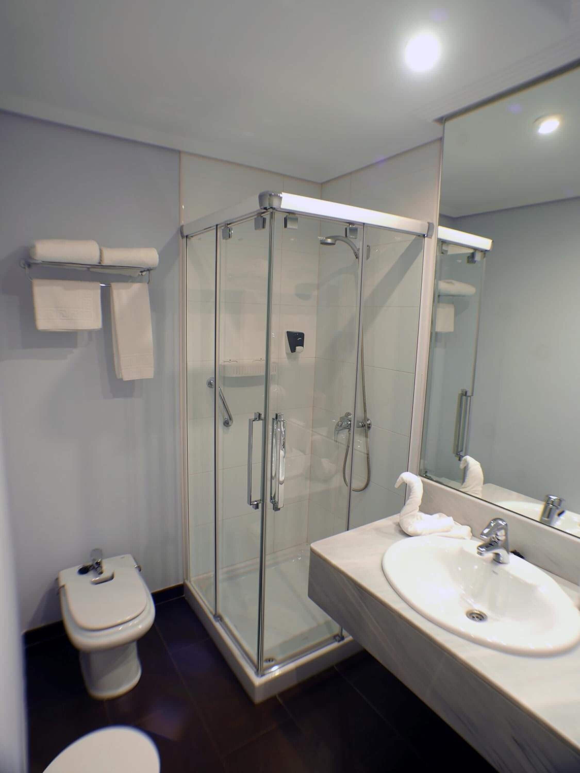 Un baño moderno con ducha de vidrio, inodoro y lavamanos con espejo.