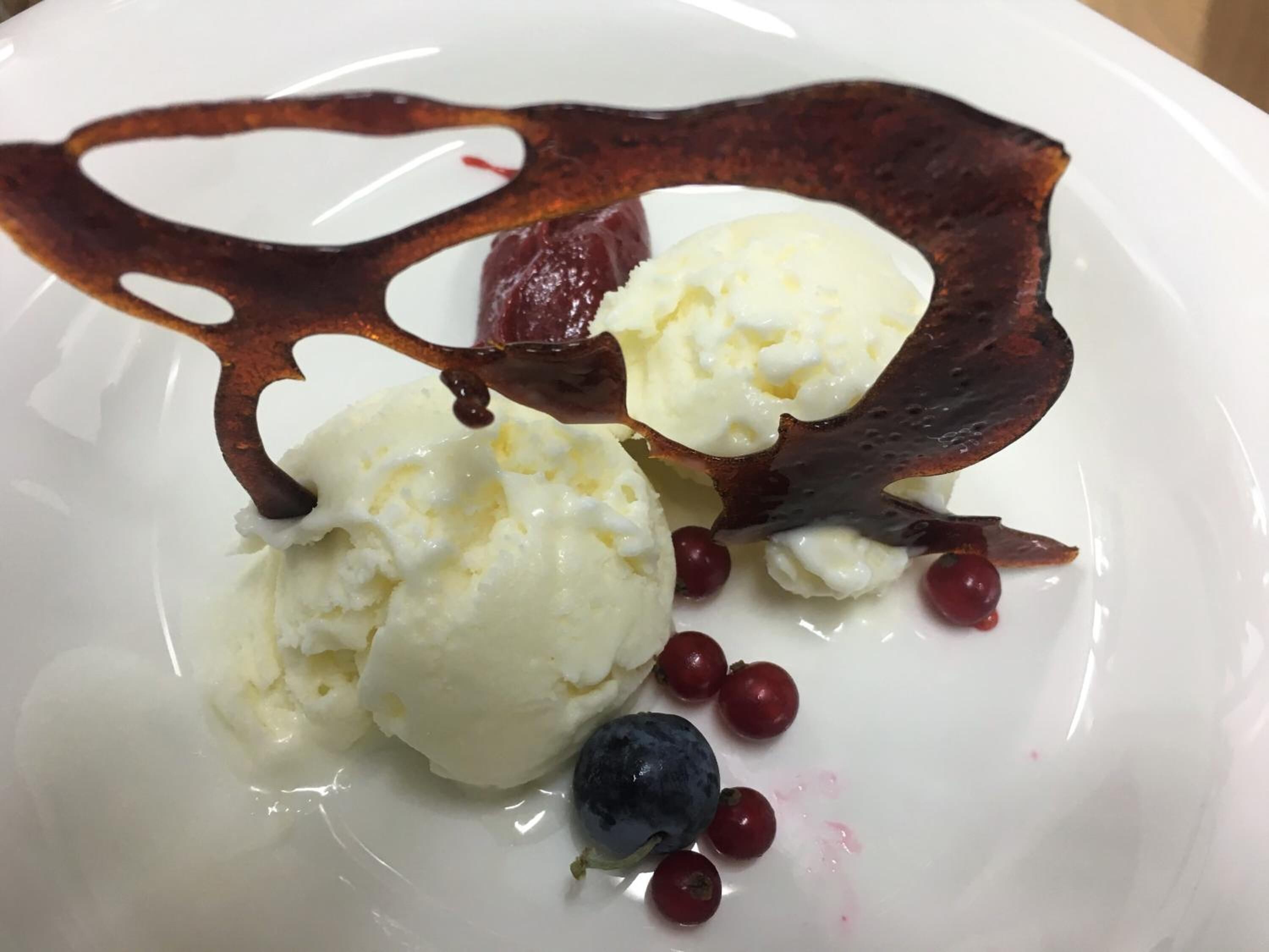 Un piatto dessert con palline di gelato, frutti di bosco e decorazioni al cioccolato.