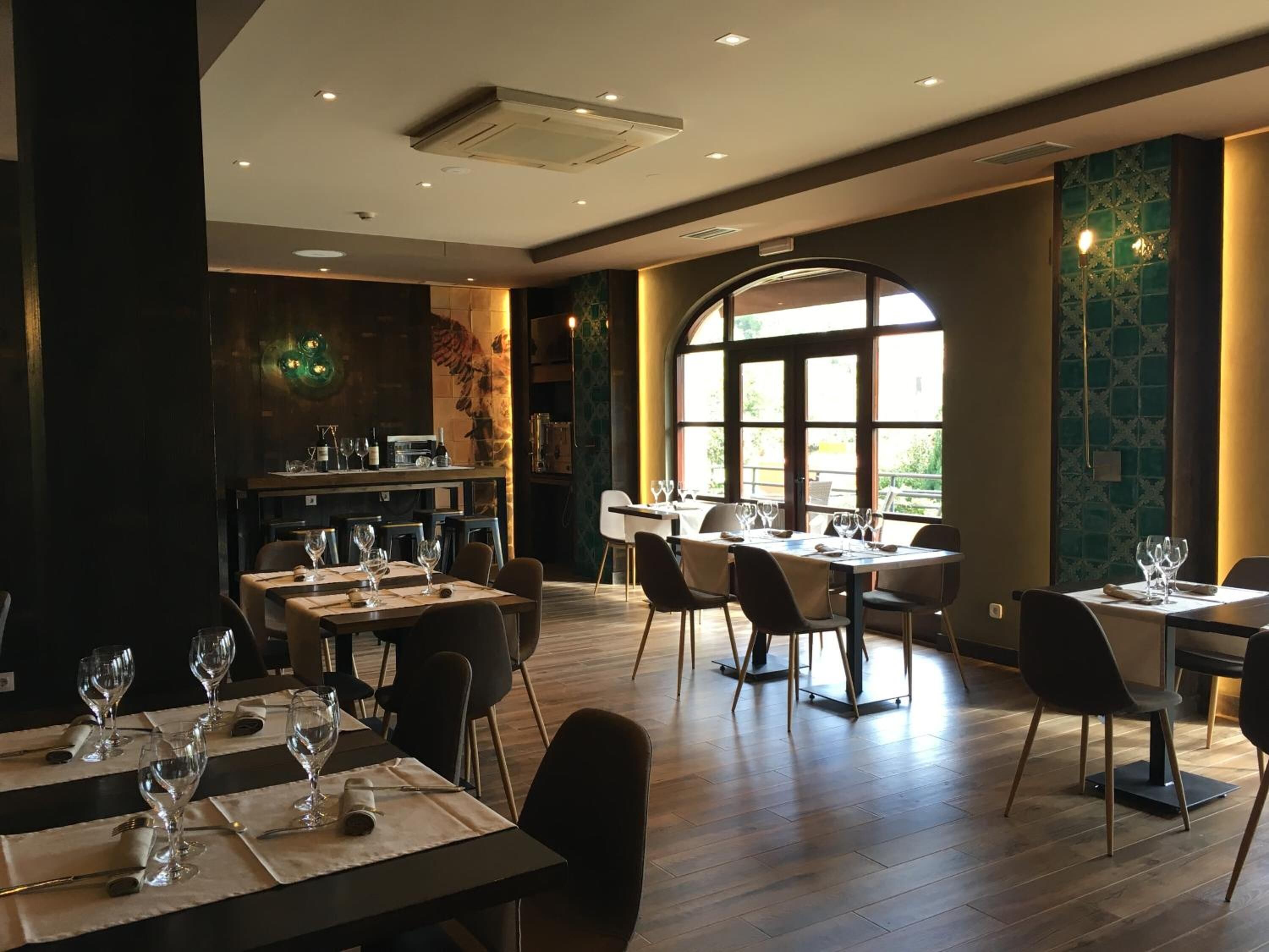 Un restaurante con varias mesas, sillas y un amplio ventanal que permite la entrada de luz natural.