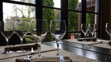 Mesa dispuesta con copas de vino y cubiertos, con vistas a árboles y un edificio a través de amplias ventanas.