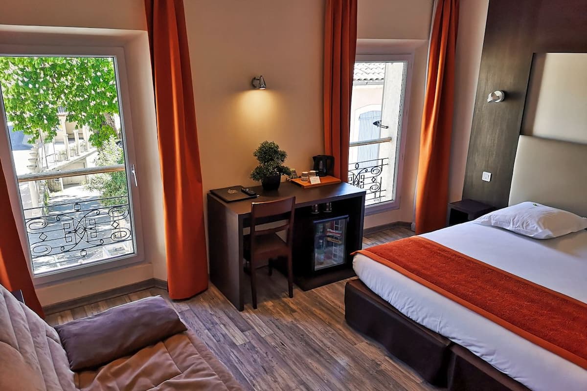 Een hotelkamer met een bed, een bureau met stoel, een kleine koelkast en een raam met gordijnen.