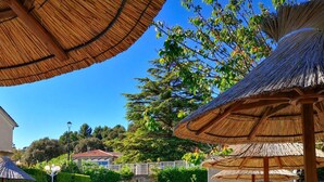 Área de piscina com espreguiçadeiras e guarda-sóis de palha.