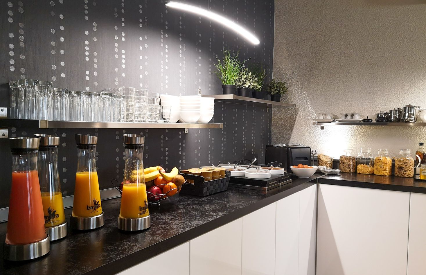 Una barra de desayuno con diferentes alimentos y bebidas, que incluye un bol de frutas, cereales y dispensadores de jugo.