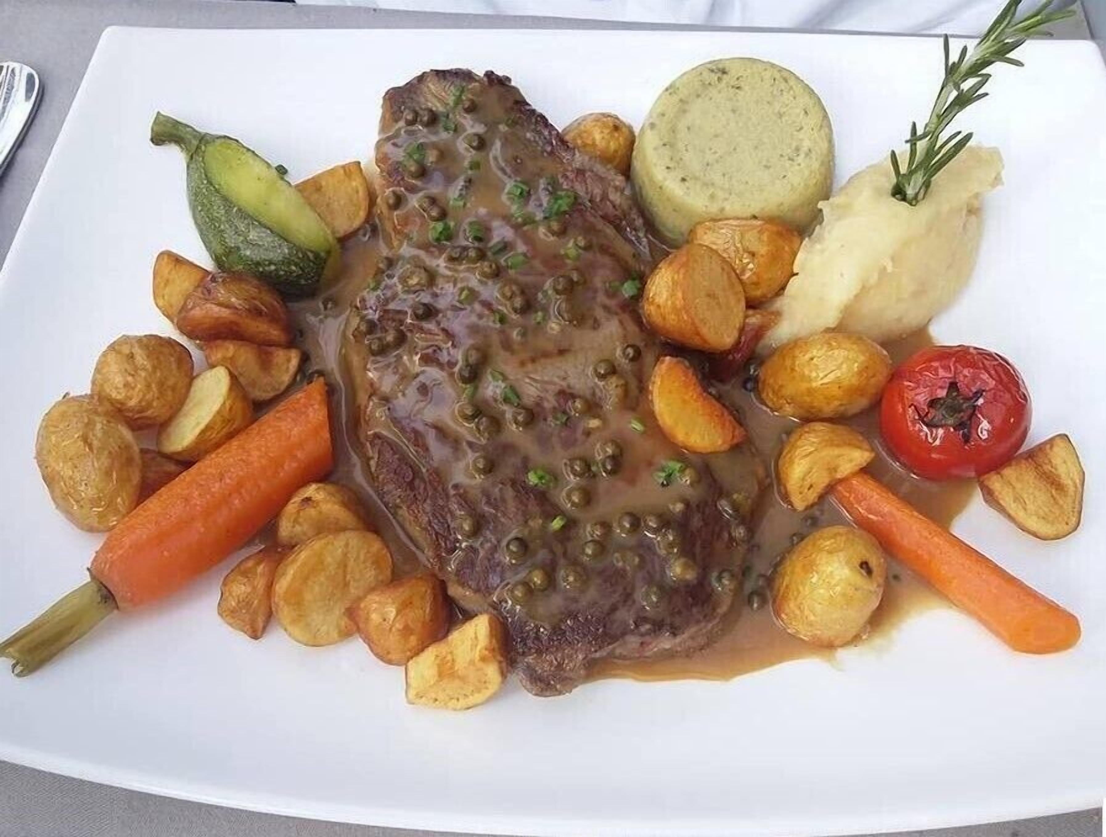 A plate with a steak, roasted potatoes, a boiled potato, a carrot, a tomato, and a cucumber.