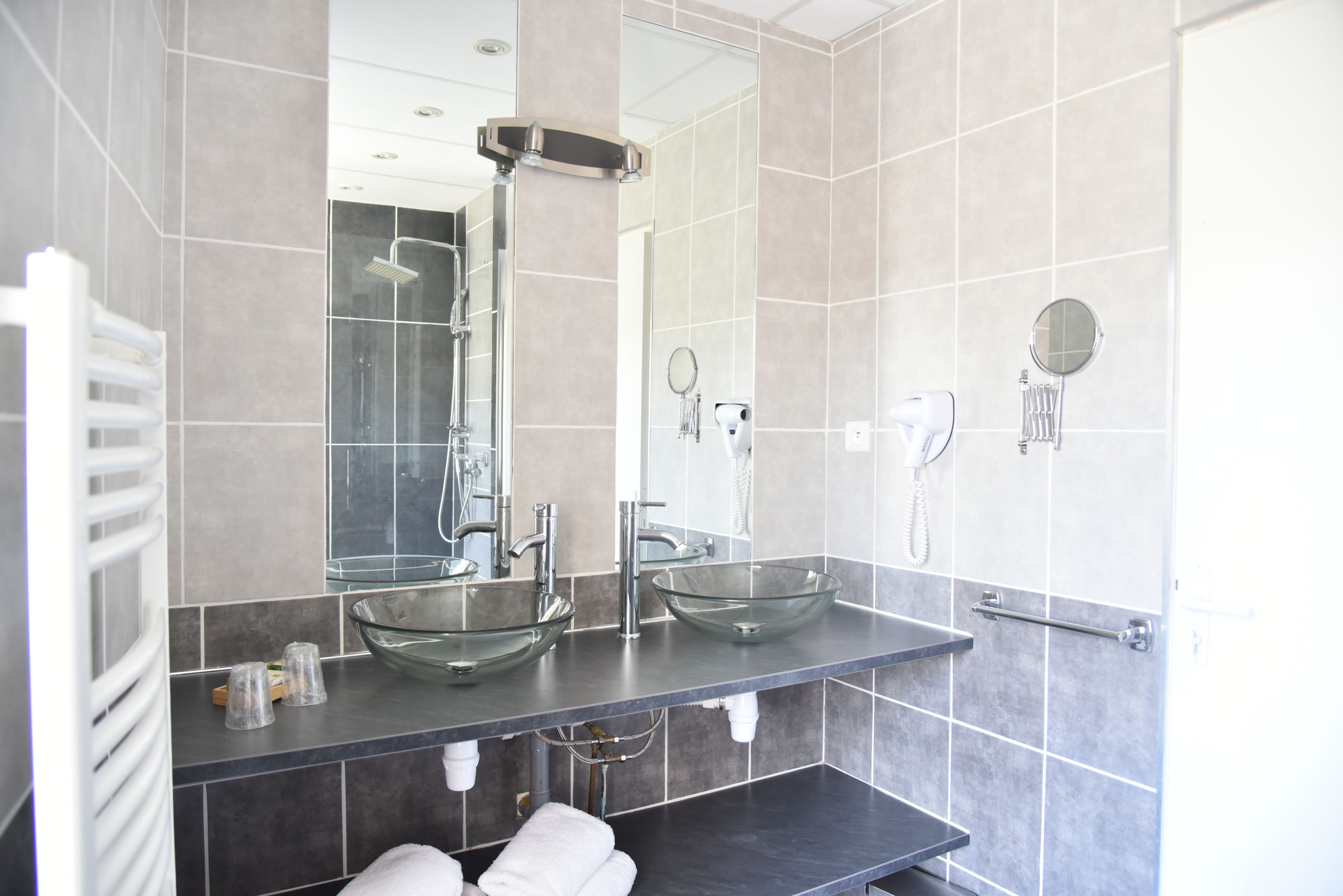 A modern bathroom with two glass sinks, a large mirror, a shower, and a towel rack.