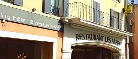 Un edificio con un cartel que indica 'RESTAURANT LES ALPES' y otro cartel que anuncia 'hotel y restaurante'.