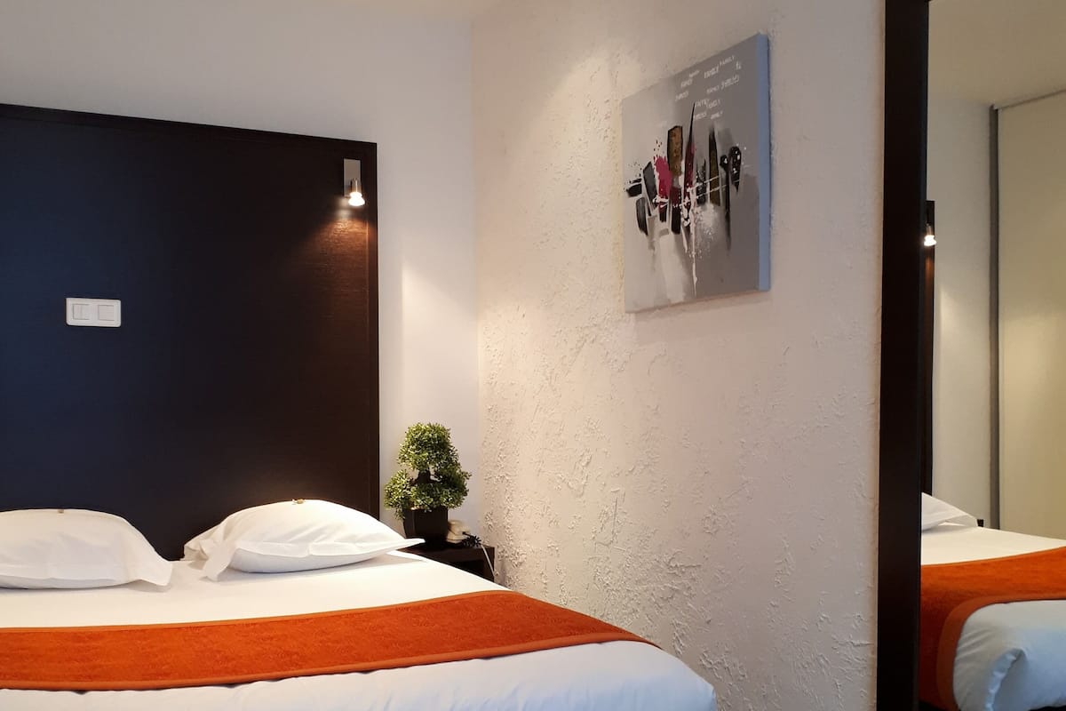 Een moderne hotelkamer met een groot bed, een donker hoofdeinde, een kleine potplant, een kunstwerk aan de muur en een grote spiegel.