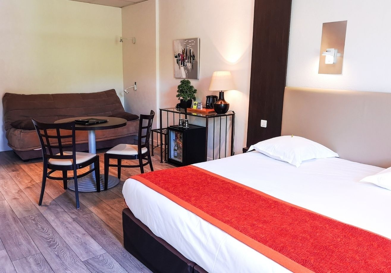 A hotel room with a bed, a desk with a chair, a sofa, and a small table with a lamp.