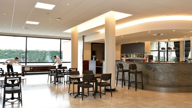 A modern restaurant with a bar area, high ceilings, and large windows. - Logis Lyon Est (Saint-Maurice-de-Beynost)