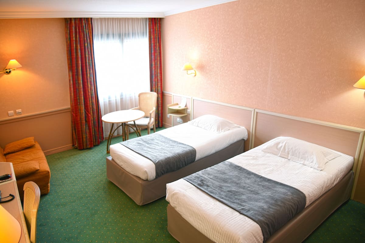 Una habitación de hotel con dos camas individuales, una mesita, una silla y un escritorio con lámpara.
