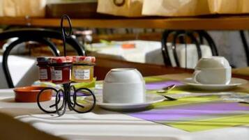 Una mesa con mantel blanco, dos tazas blancas, un frasco de mermelada y un recipiente naranja pequeño.