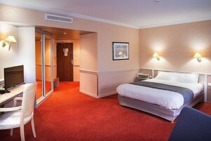 Habitación de hotel con cama, escritorio con computadora, silla y dos lámparas de pared.