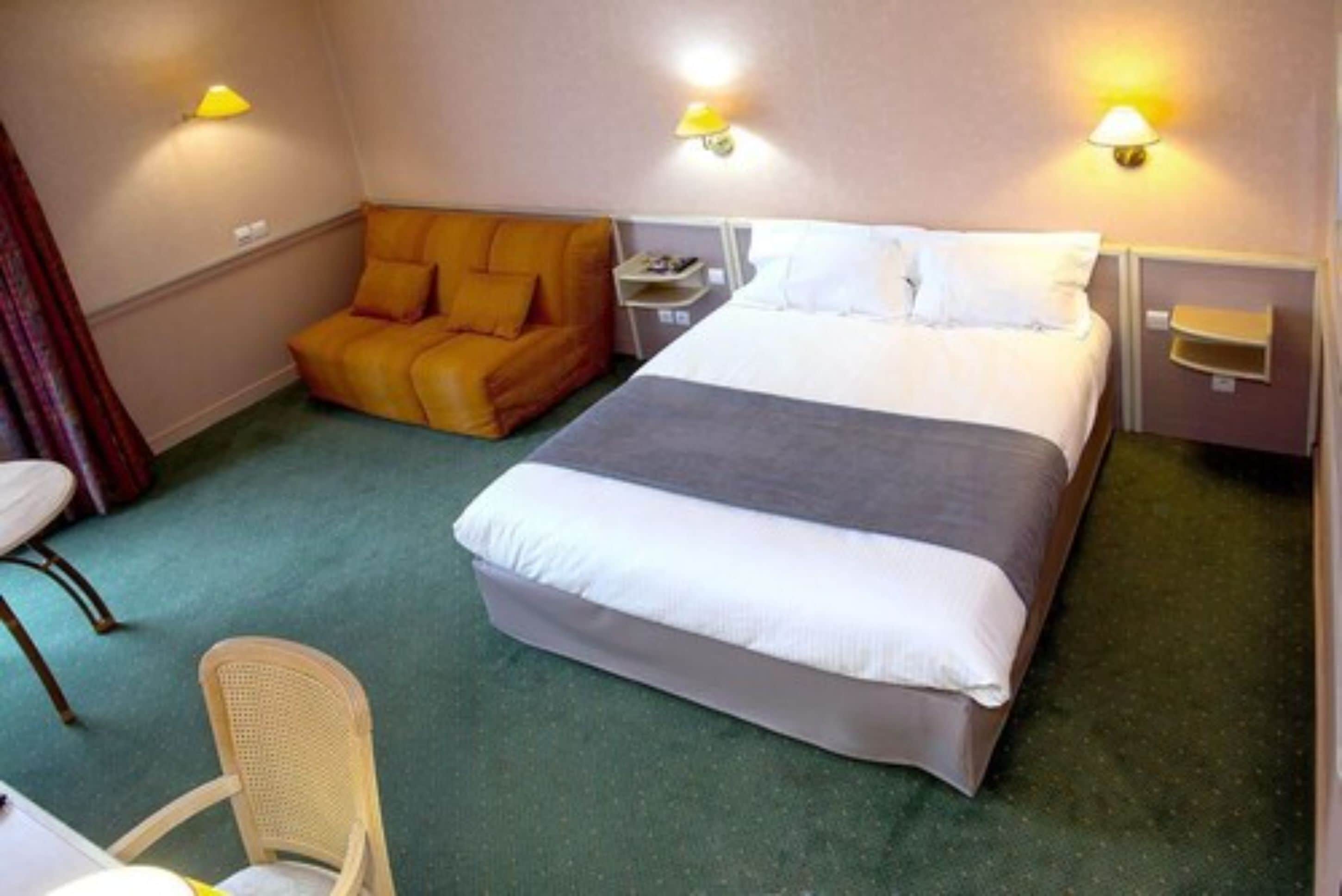 A hotel room with a bed, a chair, a small table, and a lamp.
