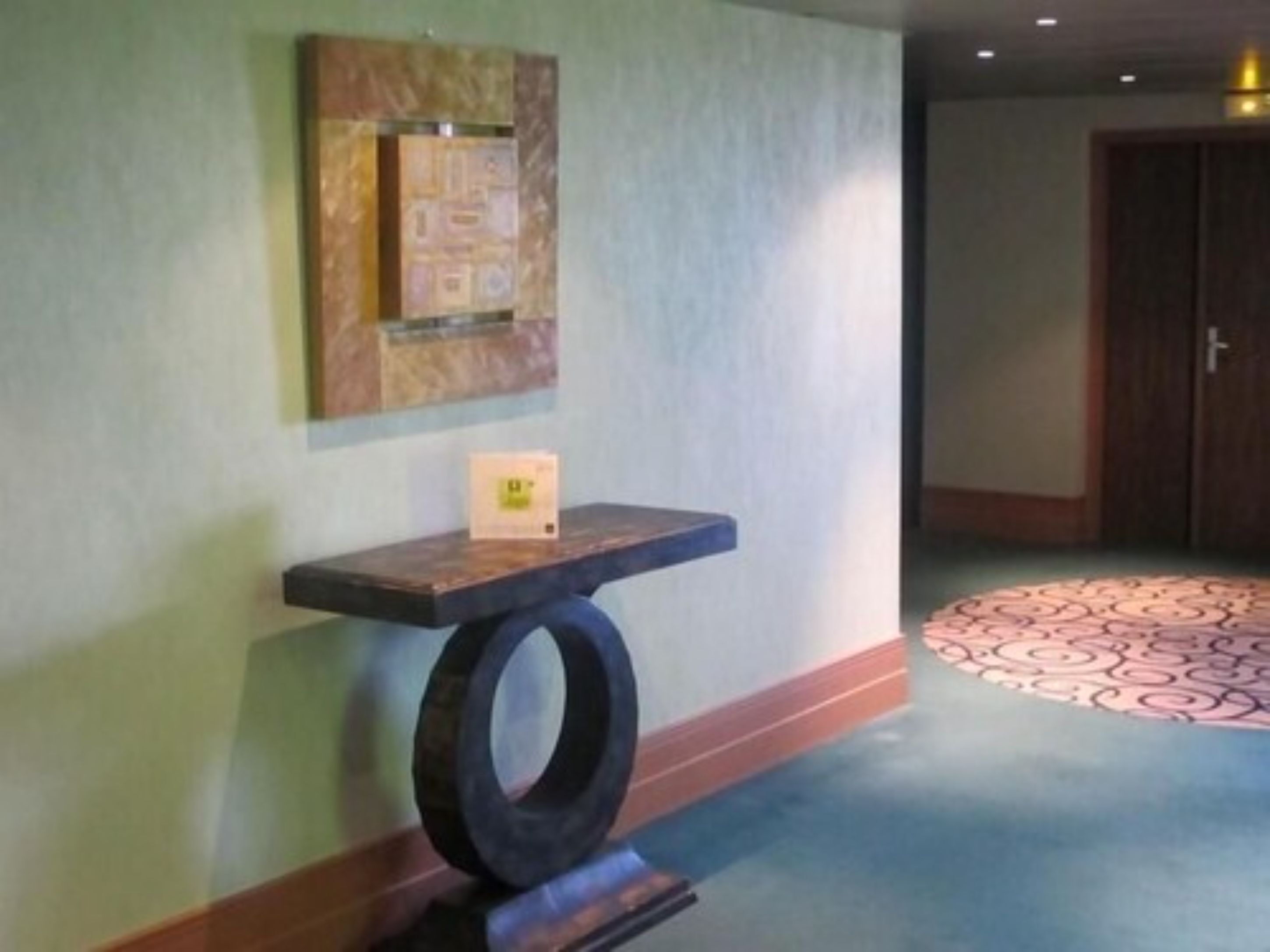 A hallway with a decorative wall panel, a small table with a box, and a patterned carpet.