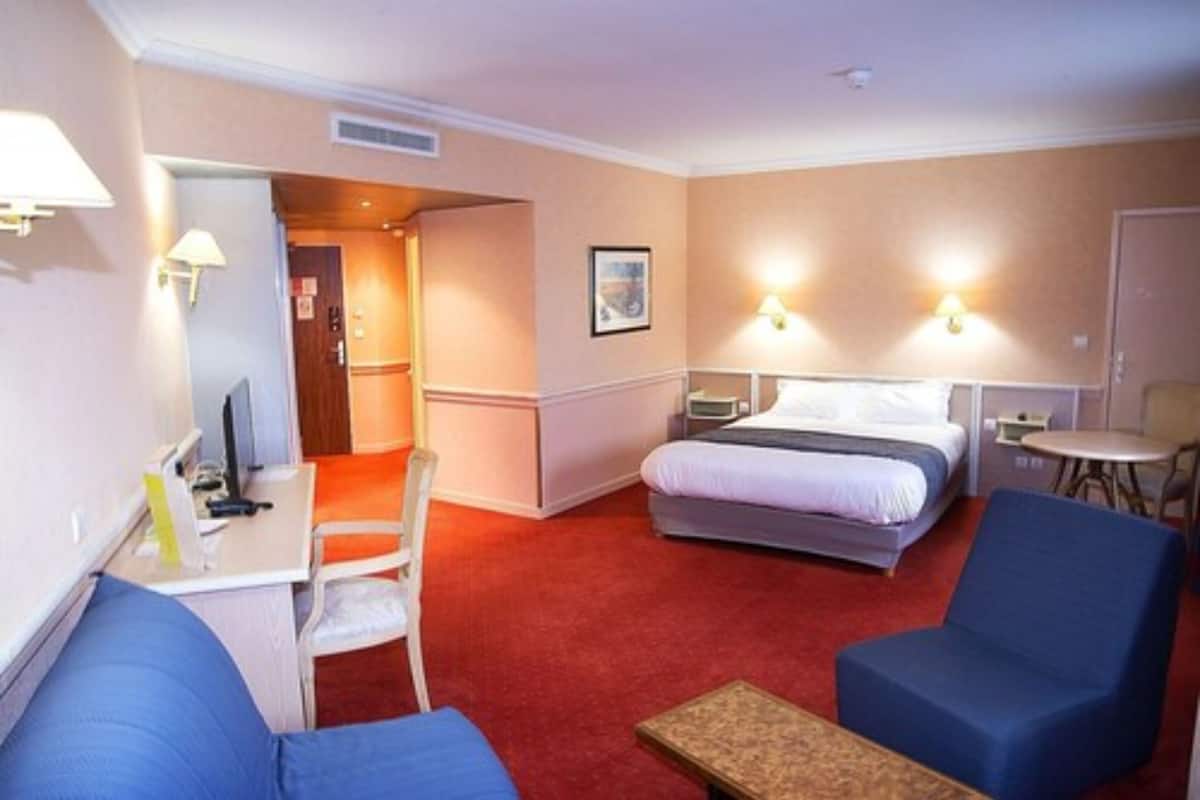 Una habitación de hotel con cama, escritorio, silla y una mesita.
