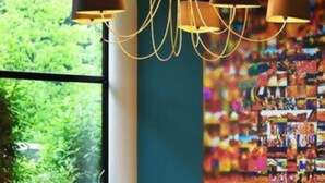 A modern interior with a large window, orange seating, and a colorful abstract wall art. - Logis Lyon Est (Saint-Maurice-de-Beynost)