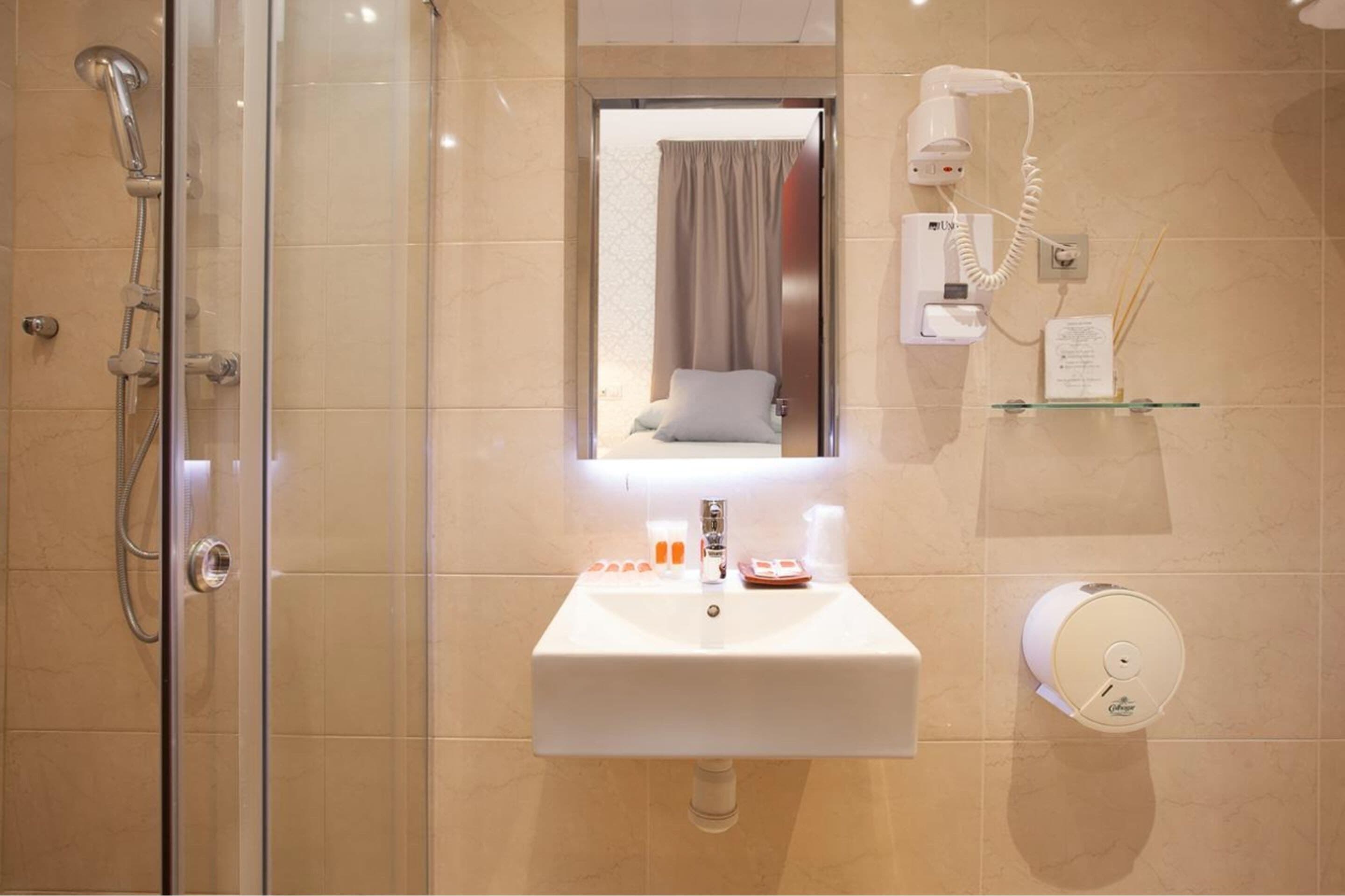Une salle de bain avec une douche en verre, un lavabo avec des articles de toilette, un sèche-cheveux et un miroir.