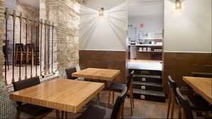 Un restaurant avec des tables et des chaises en bois, des murs en pierre et un escalier menant à un espace cuisine.