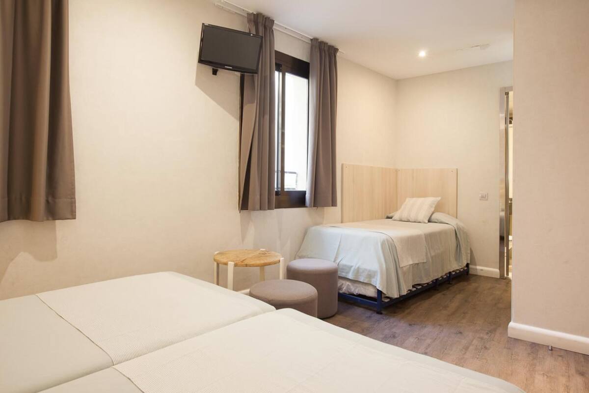 Habitación de hotel con dos camas, un televisor, un taburete pequeño y un cabecero de madera.