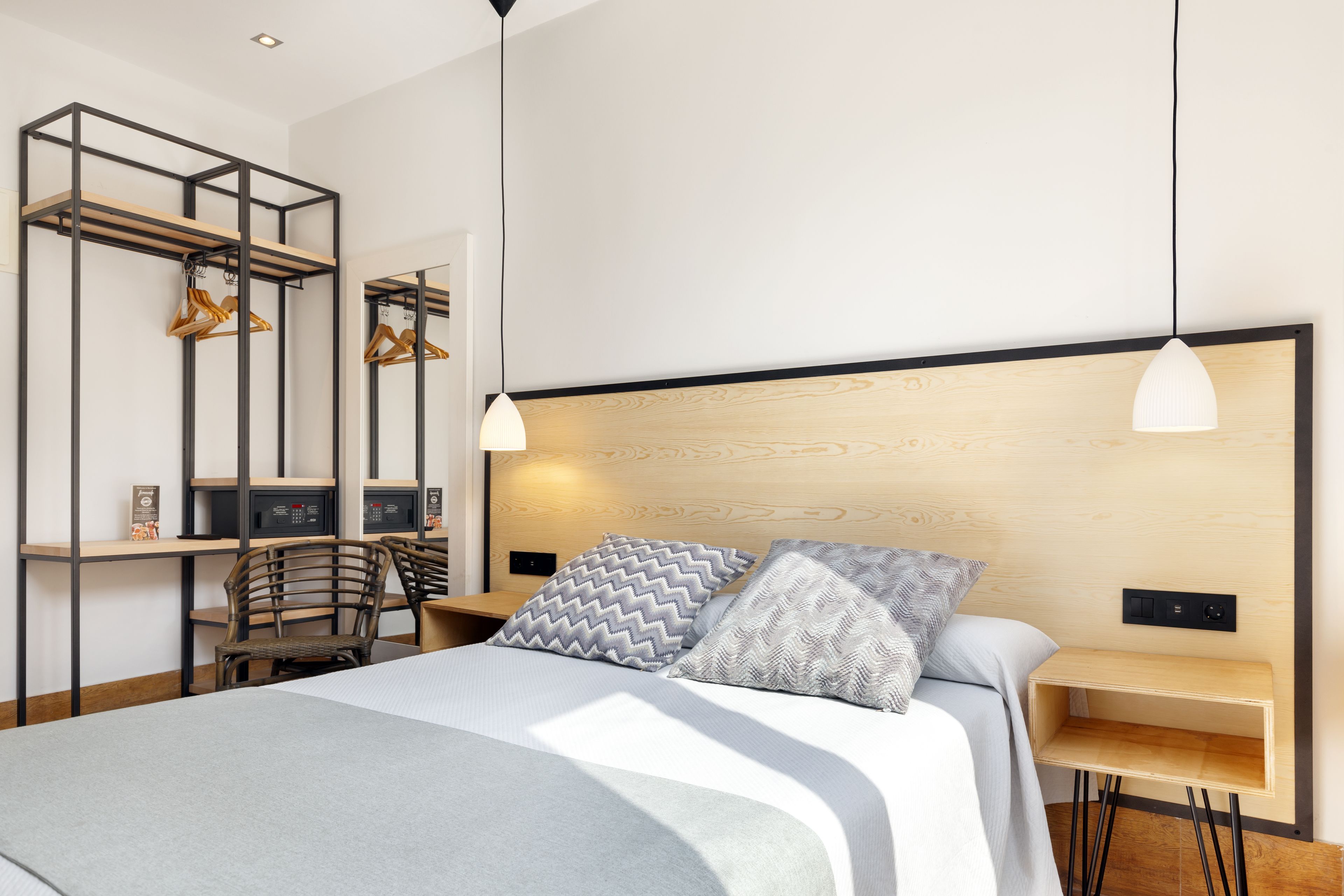 Un dormitorio moderno con cama, mesitas de noche, cabecera de madera y una unidad de estanterías empotrada con ropa.