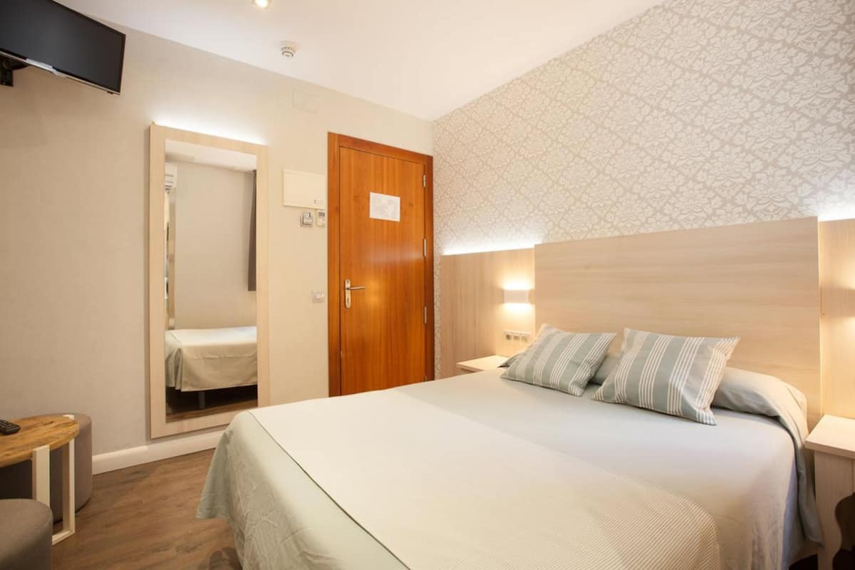 Una habitación de hotel con cama, mesita de noche y televisor montado en la pared.