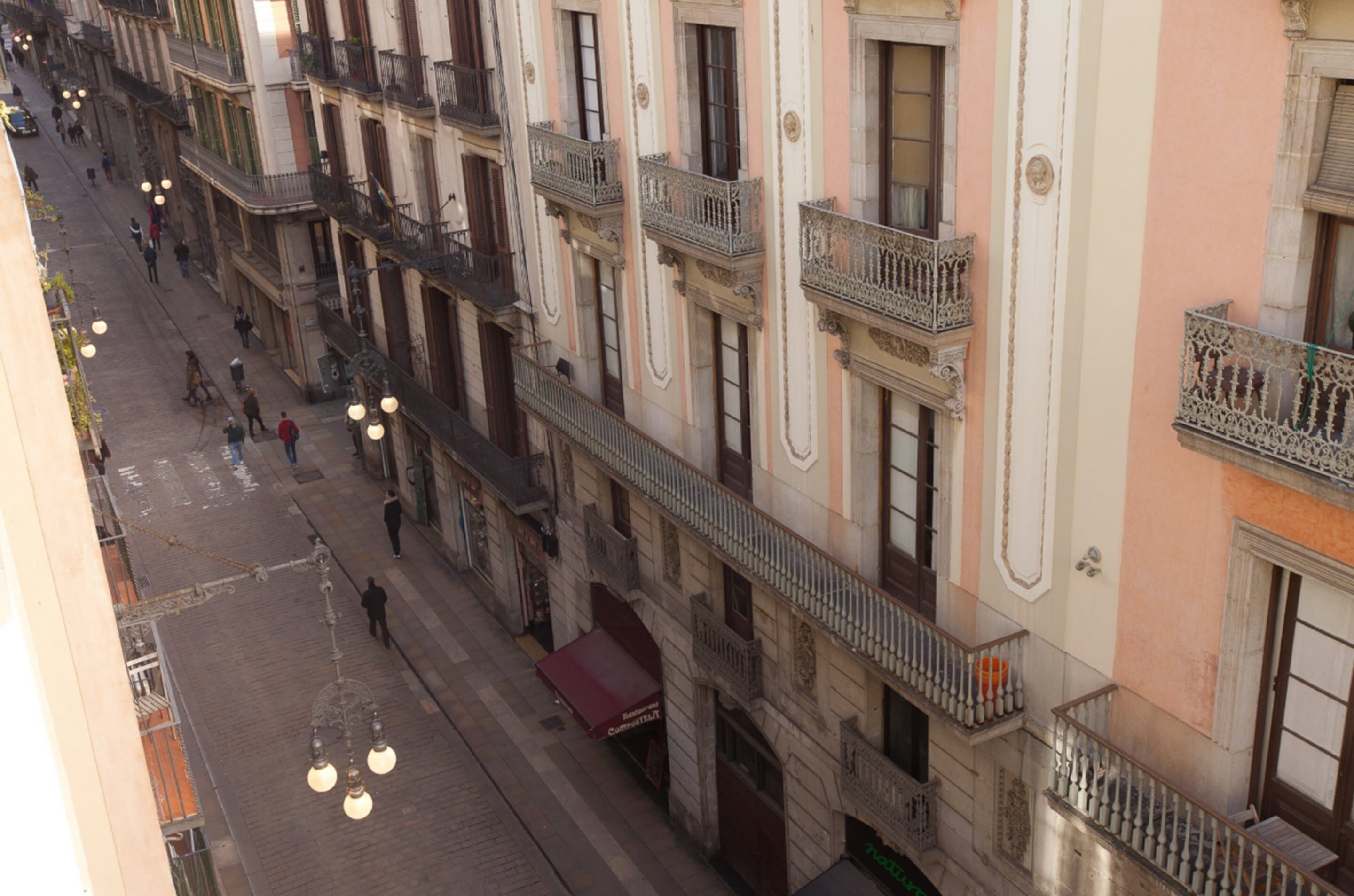 Vista de una calle con un edificio de varios balcones, un toldo rojo y farolas colgantes.