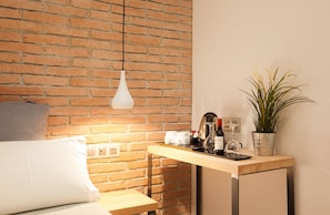 A modern room with a brick wall, a hanging light fixture, a small wooden table with a potted plant, and a bed with pillows. - Hostal Fernando (Barcelona)