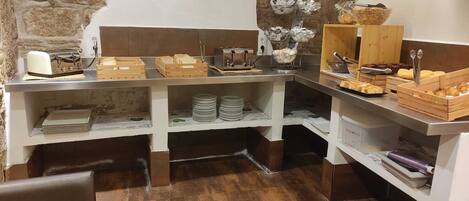 A breakfast buffet setup with various food items, a toaster, and a television mounted on the wall.