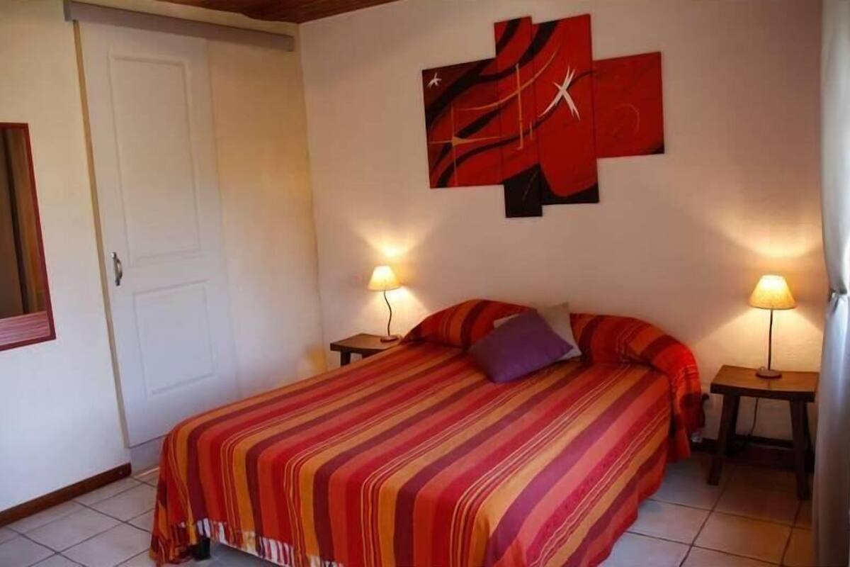 Une chambre à coucher avec un lit, deux lampes de chevet, une porte et un mur orné d’œuvres d’art abstraites.