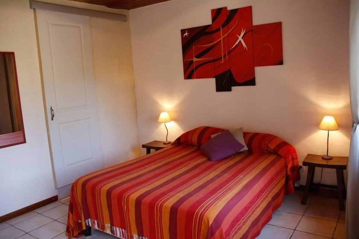 Une chambre à coucher avec un lit, deux lampes de chevet, une porte et un mur orné d’œuvres d’art abstraites.