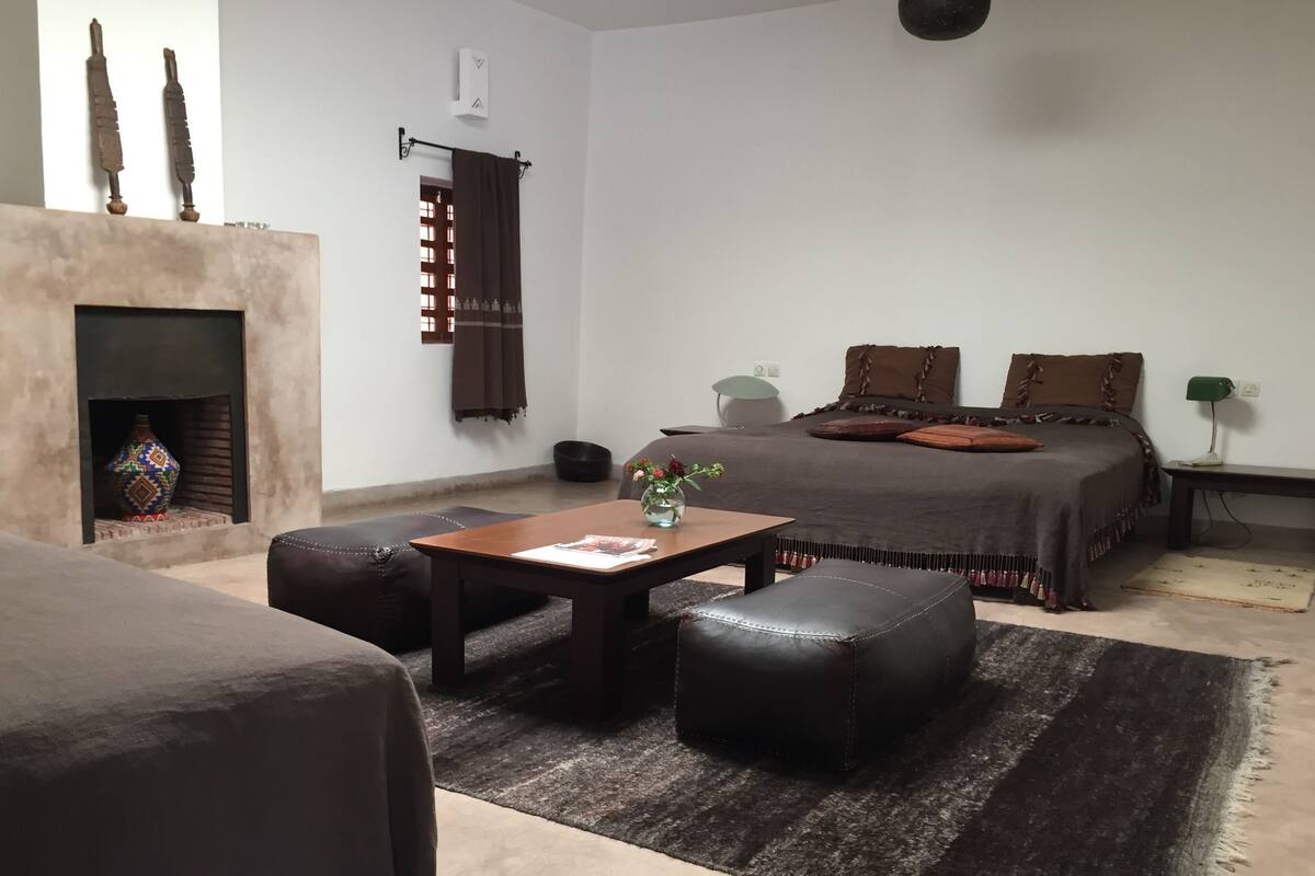 Een gezellige kamer met een bed, een tafeltje met een vaas, een open haard en een bank.