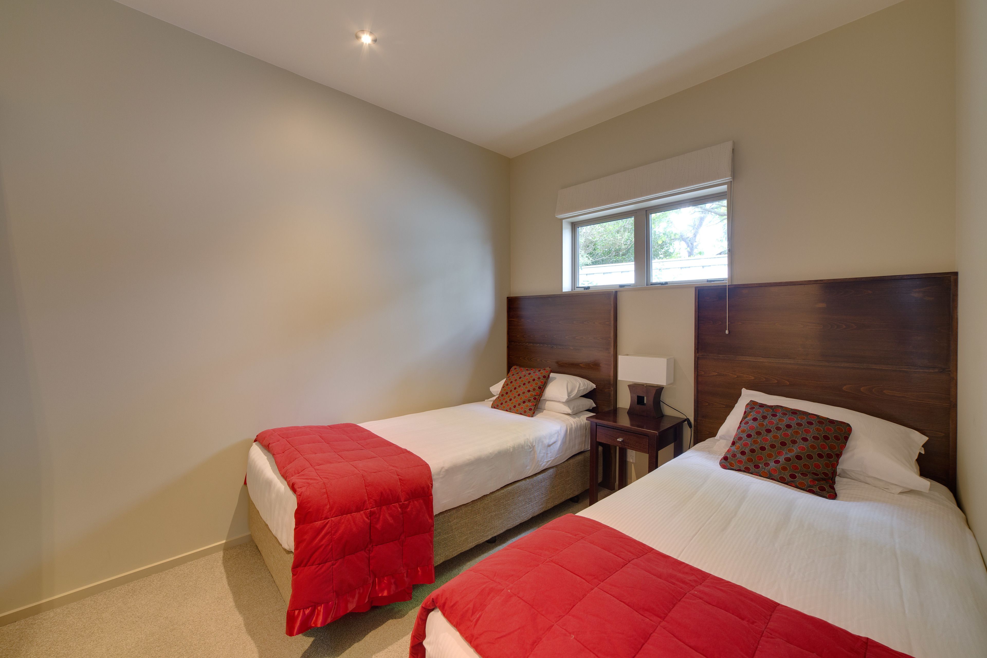 A hotel room with two beds, each with a red blanket and a wooden headboard.