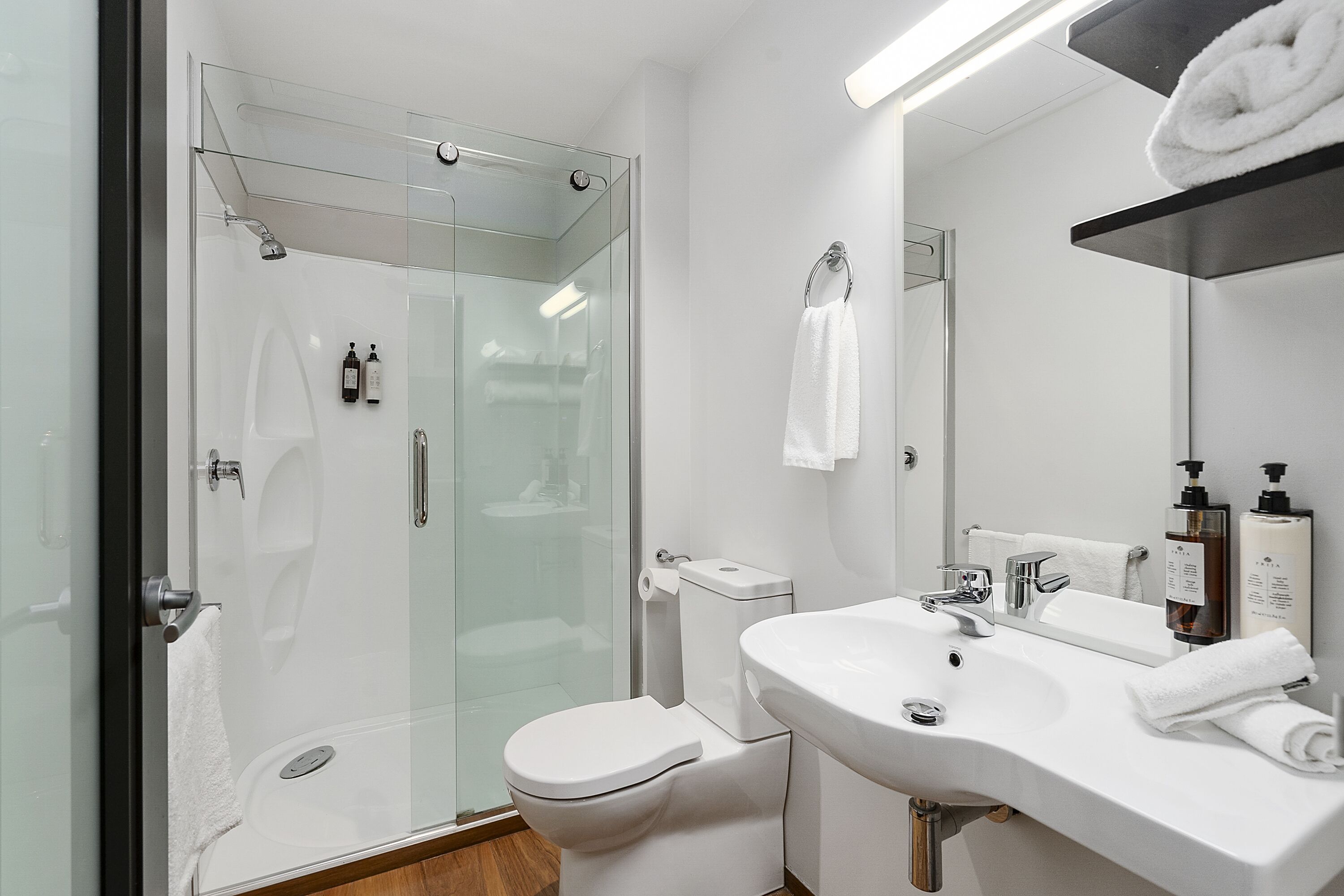 Et moderne badeværelse med en glasafskærmet brusekabine, et hvidt toilet og en vask med spejl.