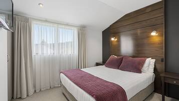 Moderni hotellihuone, jossa on suuri sänky, puinen pääty ja yöpöytä.