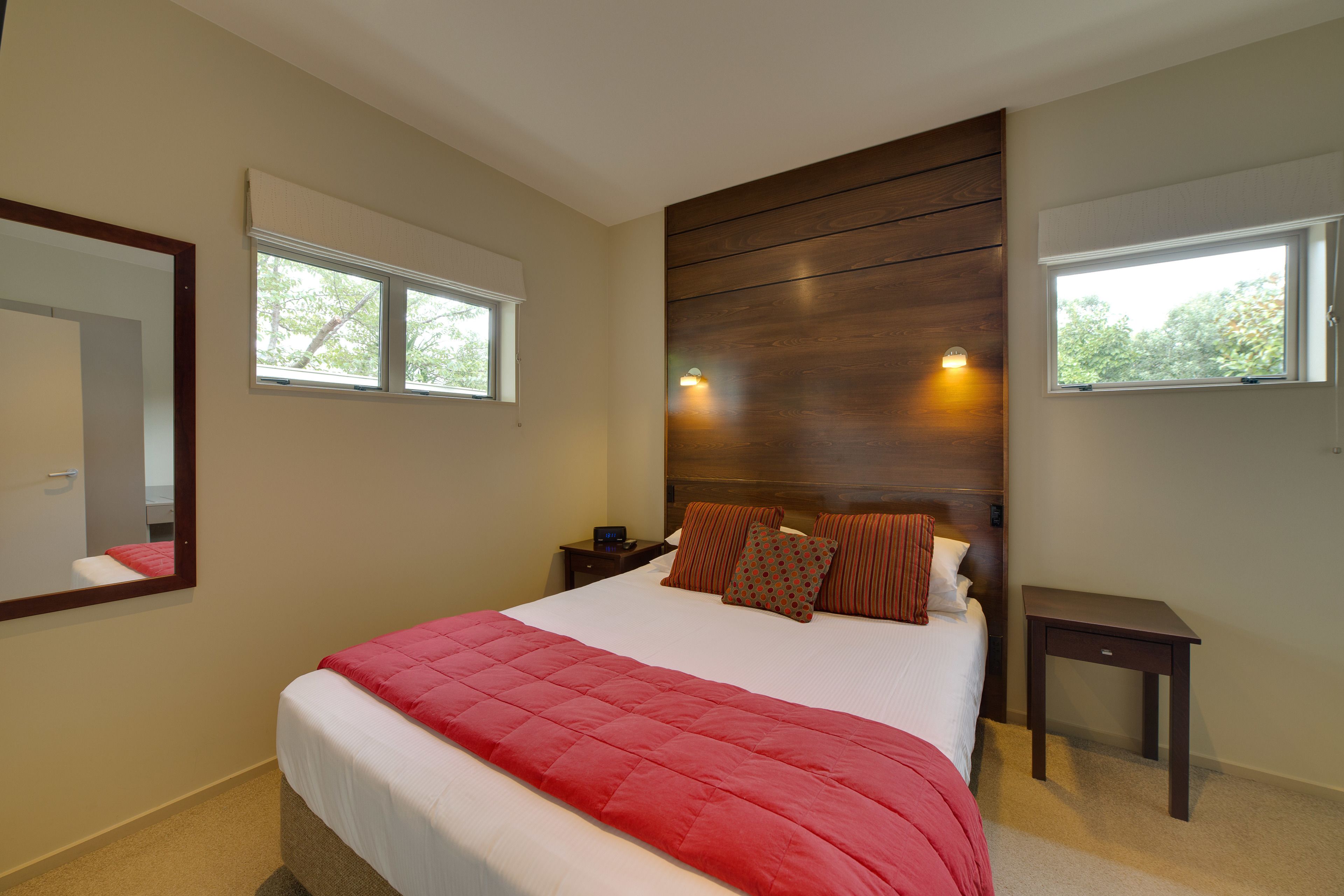 Un dormitorio con una cama grande, dos mesitas de noche, un cabecero de madera y dos ventanas.