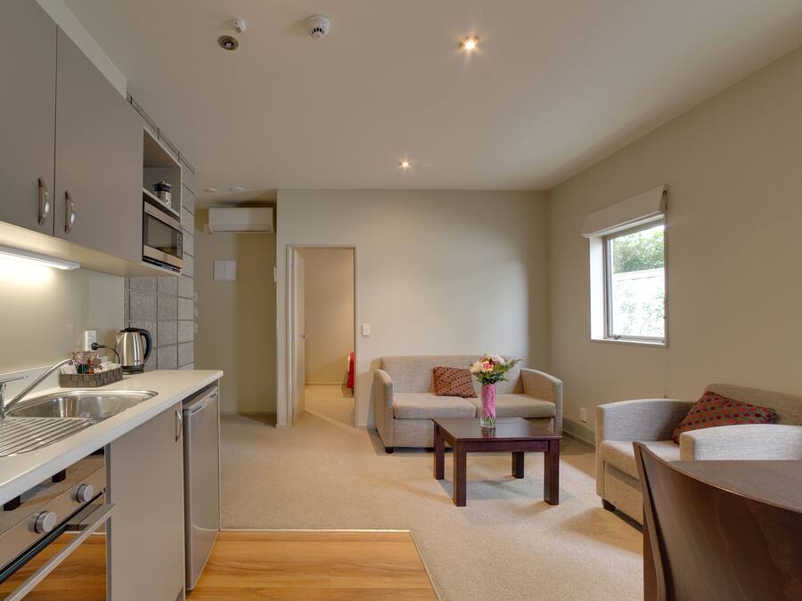 Una cocina moderna con electrodomésticos integrados, una zona de comedor con una mesa y sillas de madera, y una sala de estar con un sofá y una pequeña mesa de centro.