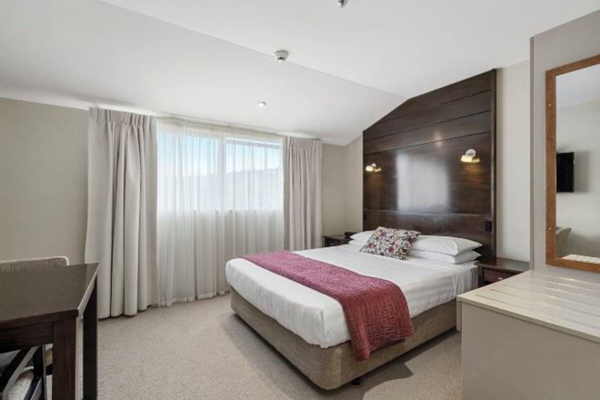 A hotel room with a large bed, a desk, a dresser, and a mirror.