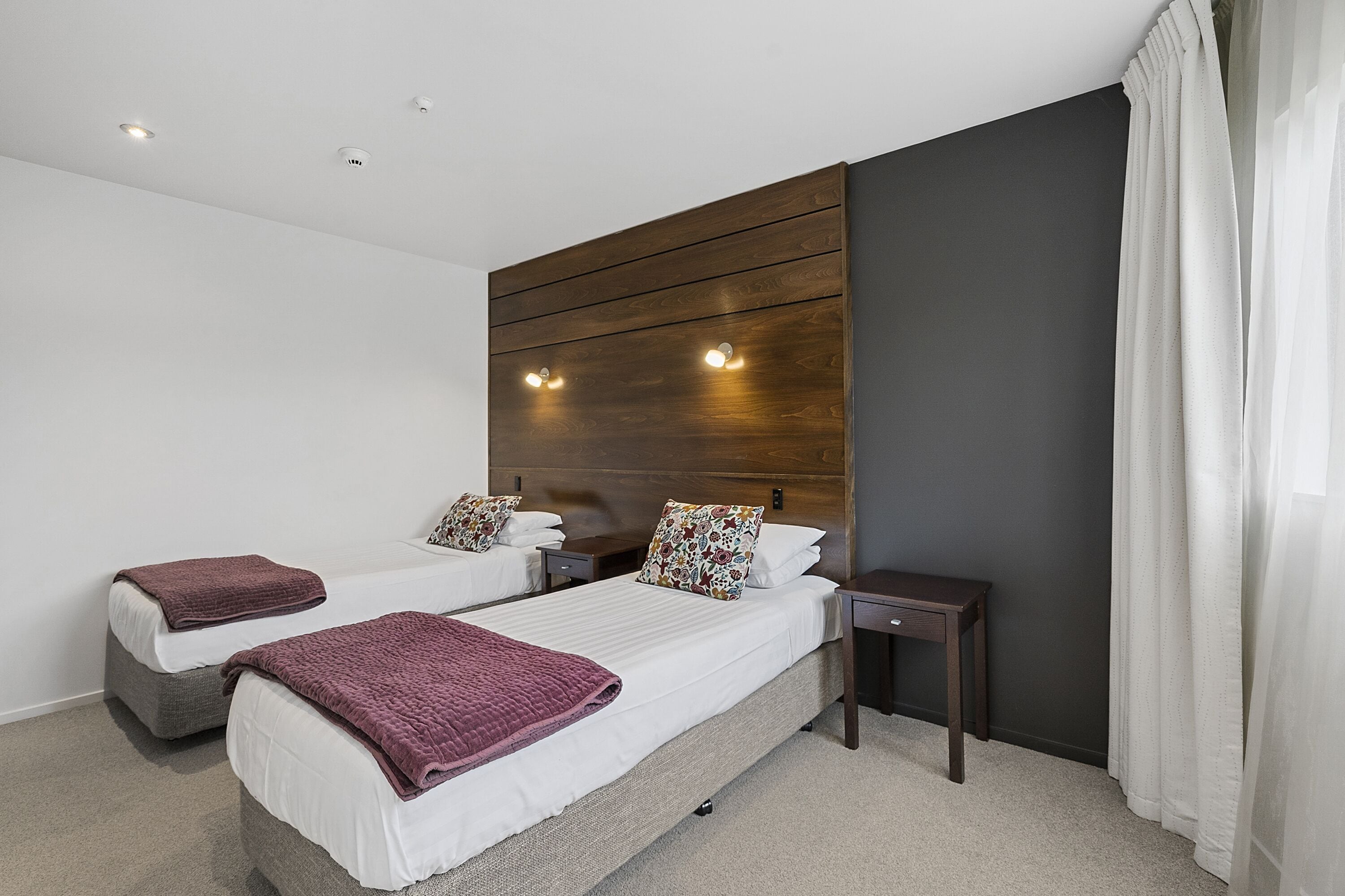 A hotel room with two beds, a wooden headboard, bedside tables, and a small nightstand.