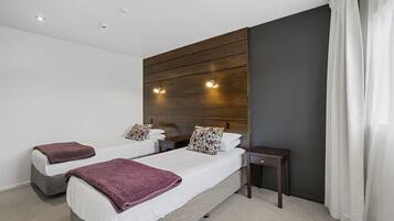 A hotel room with two beds, a wooden headboard, bedside tables, and a small nightstand.