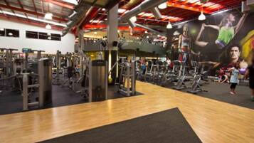 A gym with various exercise equipment, a wooden floor, and a large mural on the wall.