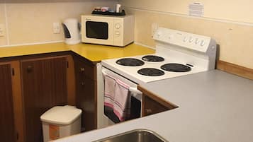 Una cocina con estufa blanca, microondas, pileta de acero inoxidable, armarios de madera y encimera amarilla.