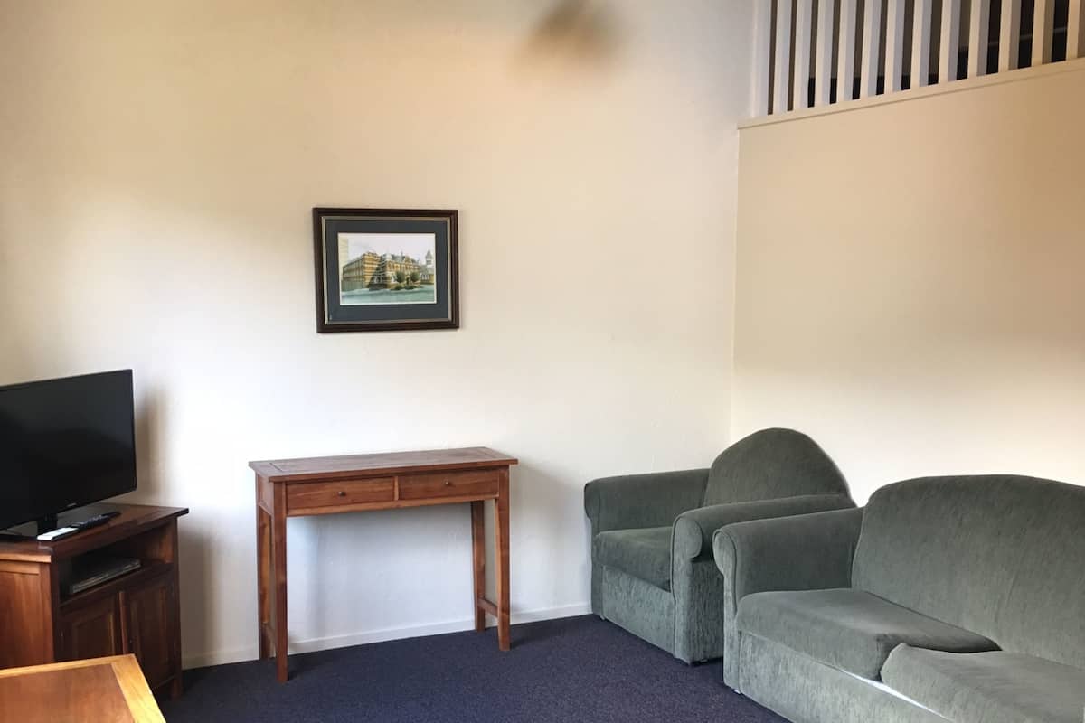 A living room with a television, a wooden desk, a green sofa, and a framed picture on the wall.